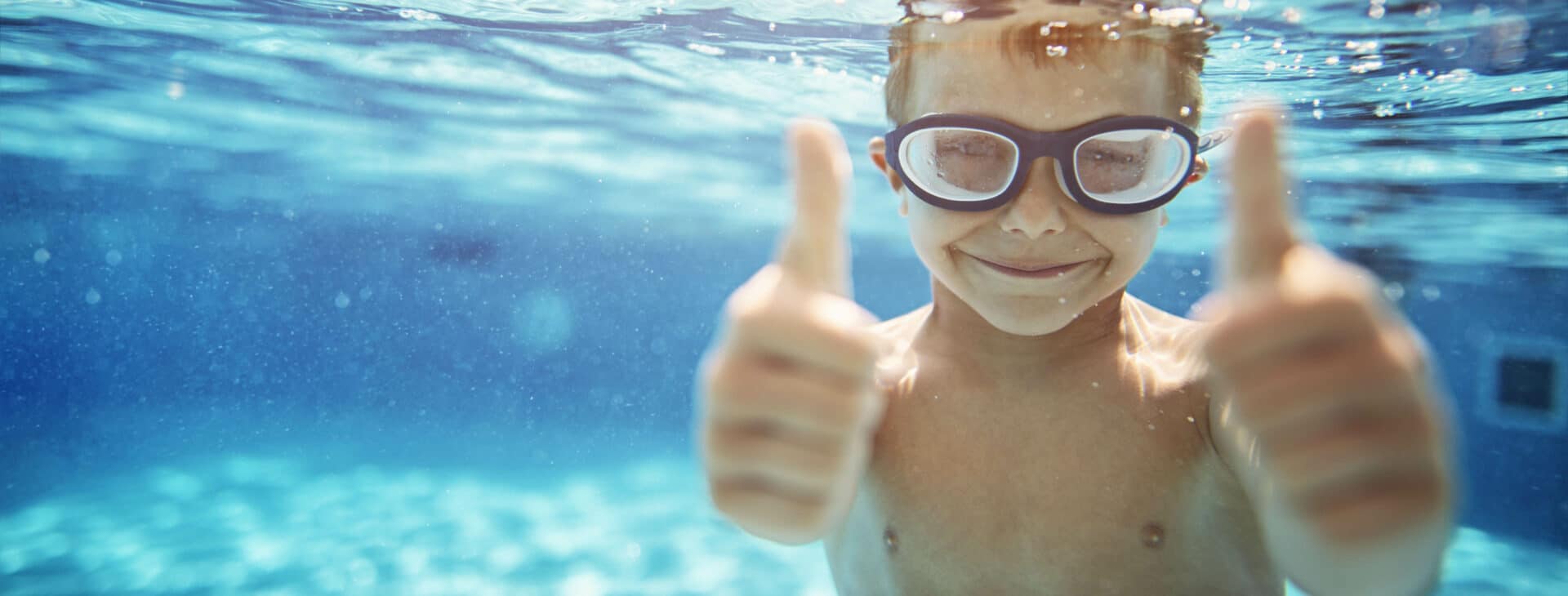 Little boy in pool showing thumbs up